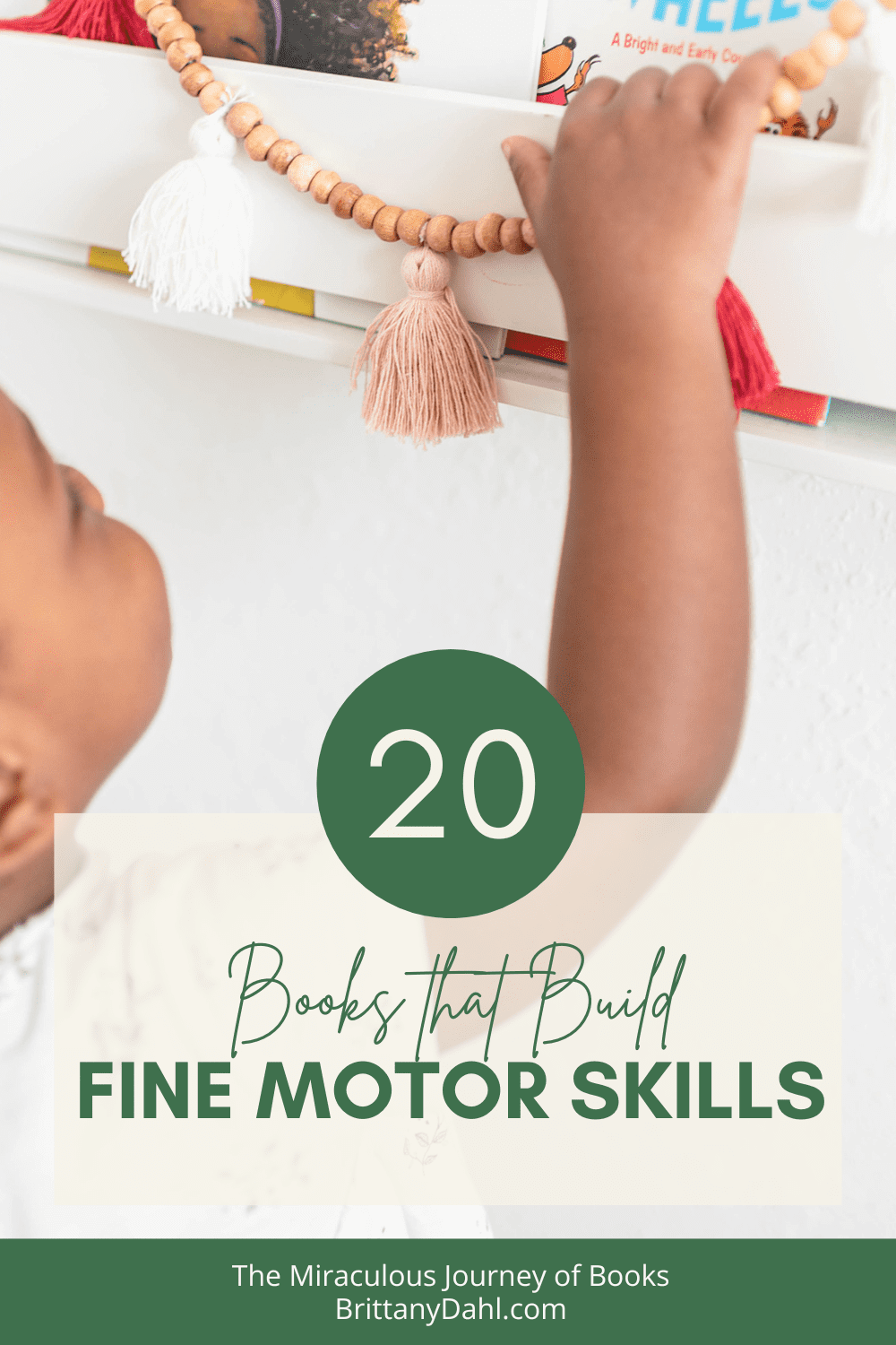 20 Fine Motor Skills Activities: Books that Build Fine Motor Skills. Image of little girl picking out a book from a forward facing shelf. It has a garland hanging on the front of it with pink and white tassels.