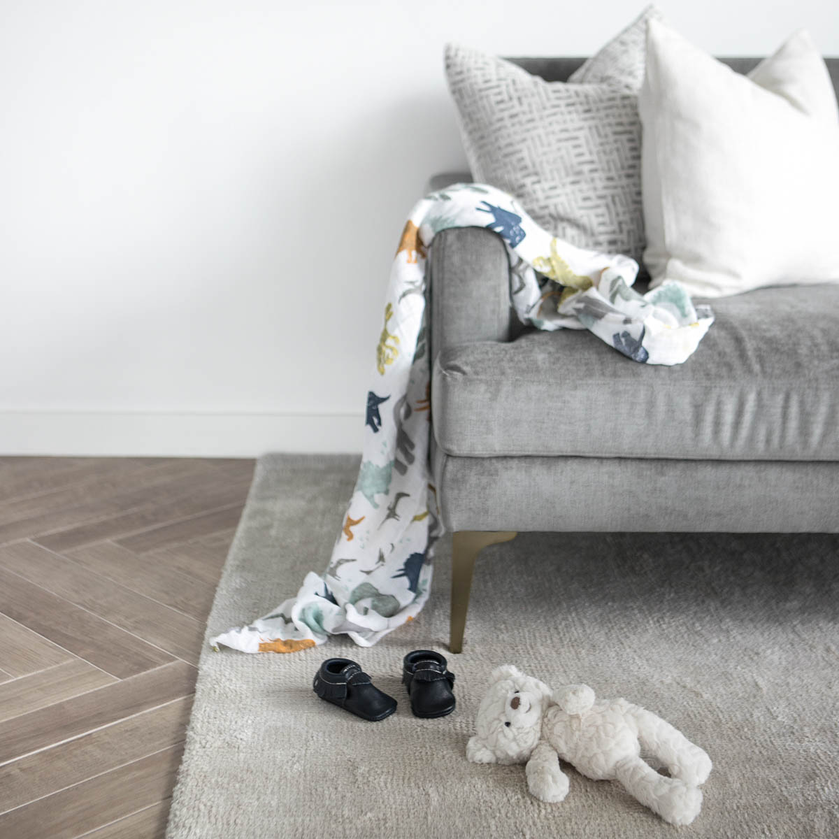 Sofa with a baby or child's blanket laying on it. Toys and a stuffed bear on the floor.