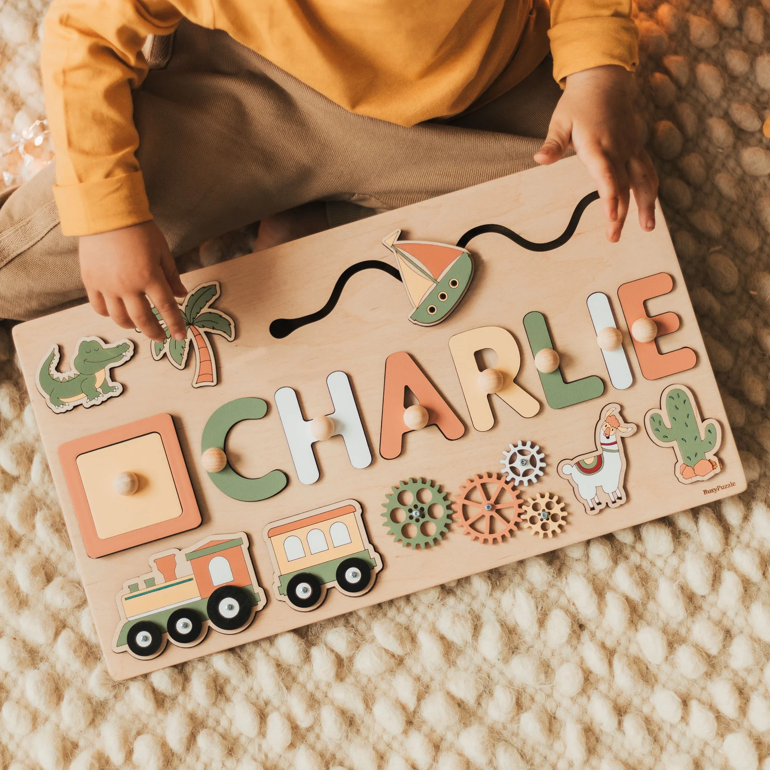 Image of child playing with busy board. Items on board include a puzzle with child's name, a train, connecting wheels.