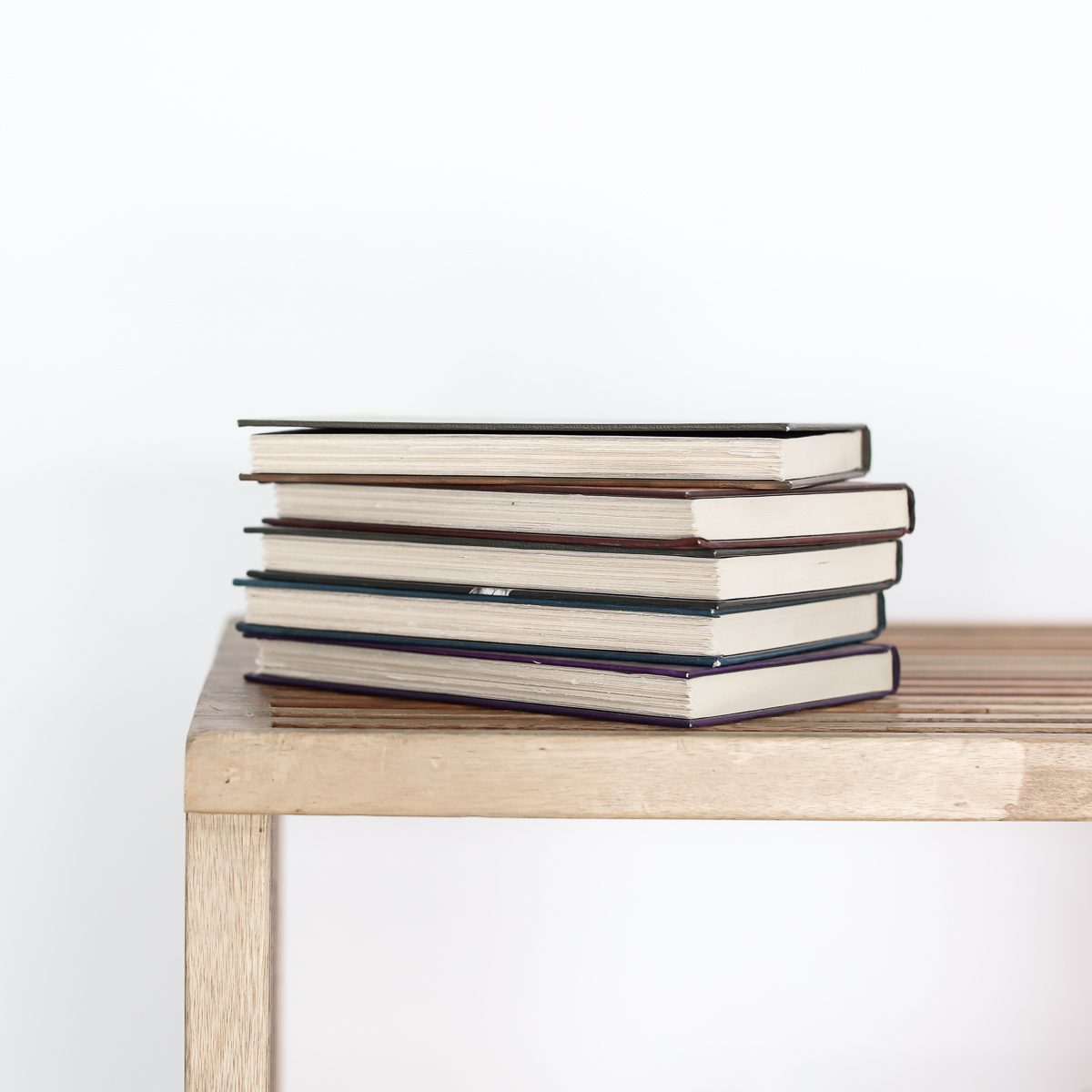 Stack of five books on a table. Spines facing away from view. Books sitting on a table.