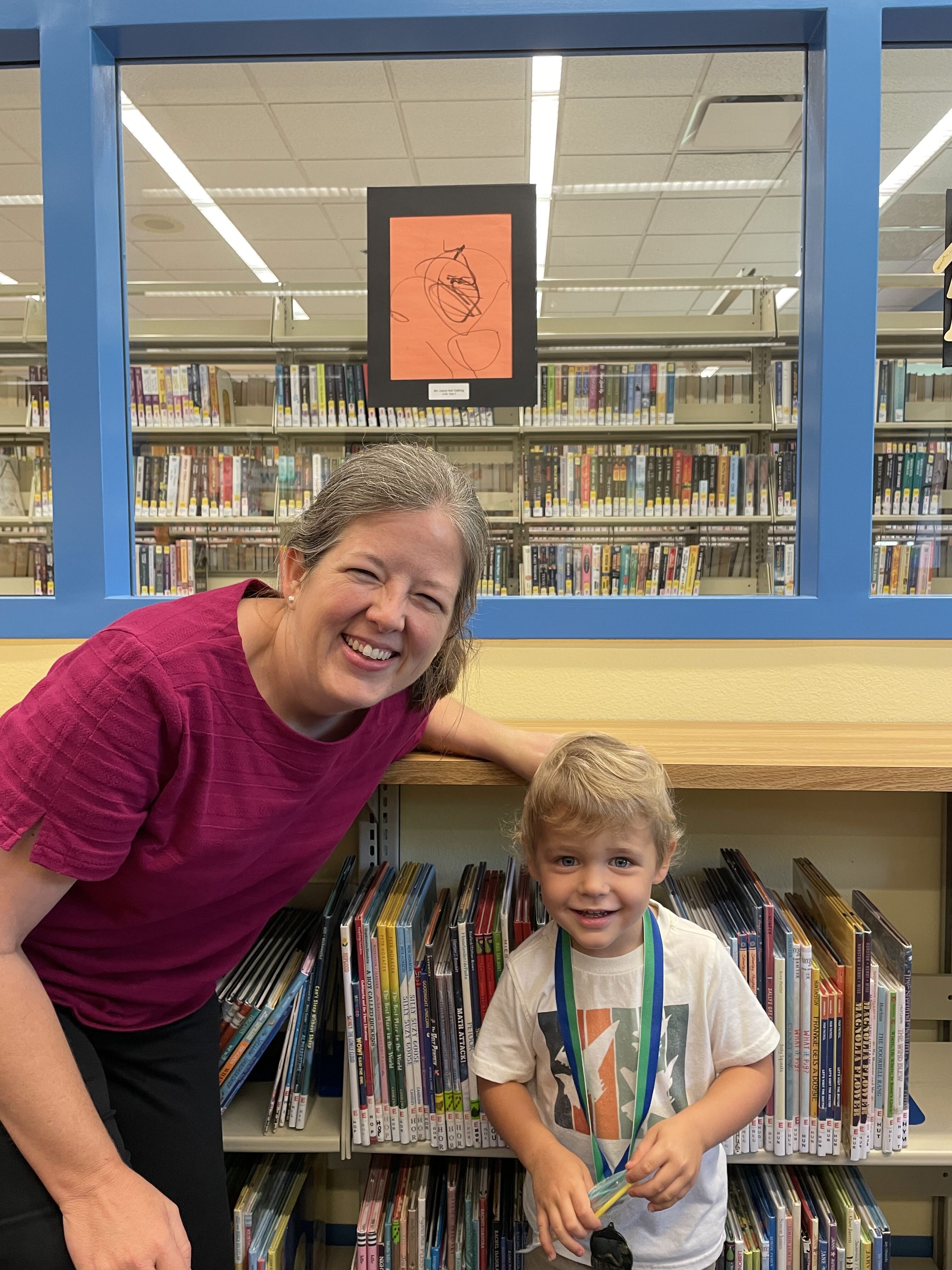Our librarian with a child in front of his art displayed on the wall of the library.