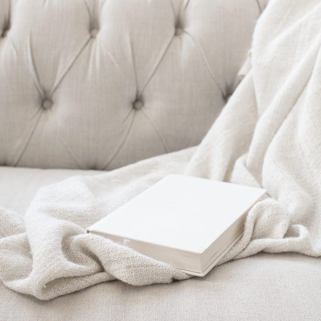Image of book lying on a blanket tossed over the arm of a couch.
