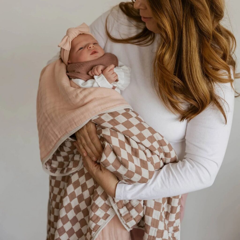 Image of woman holding a newborn that is wrapped in the ParkerBabyCo rosewood checkered quilt.