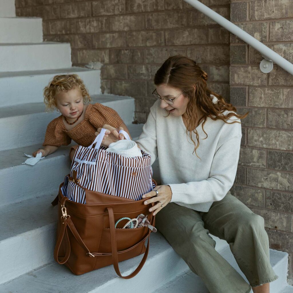 Image of woman and little girl pulling items out of the ParkerBabyCo's WIllow Tote diarper bag. They are sitting on the stairs.