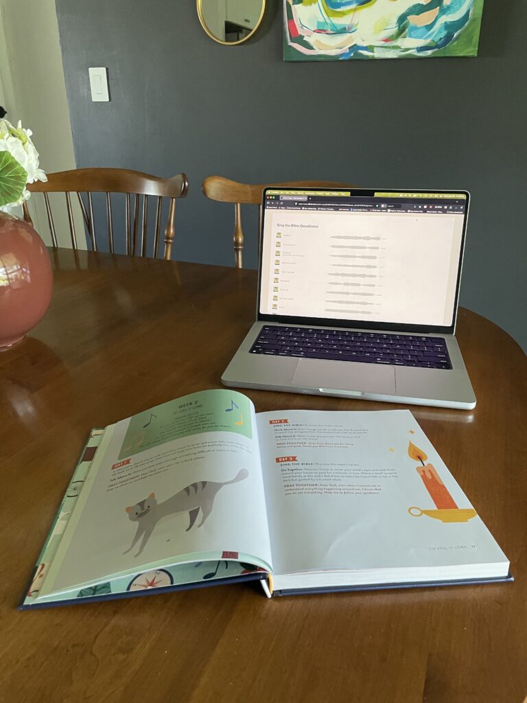Image of open book with a computer screen in the background. The screen shows the songs that you can listen to while reading the book.
