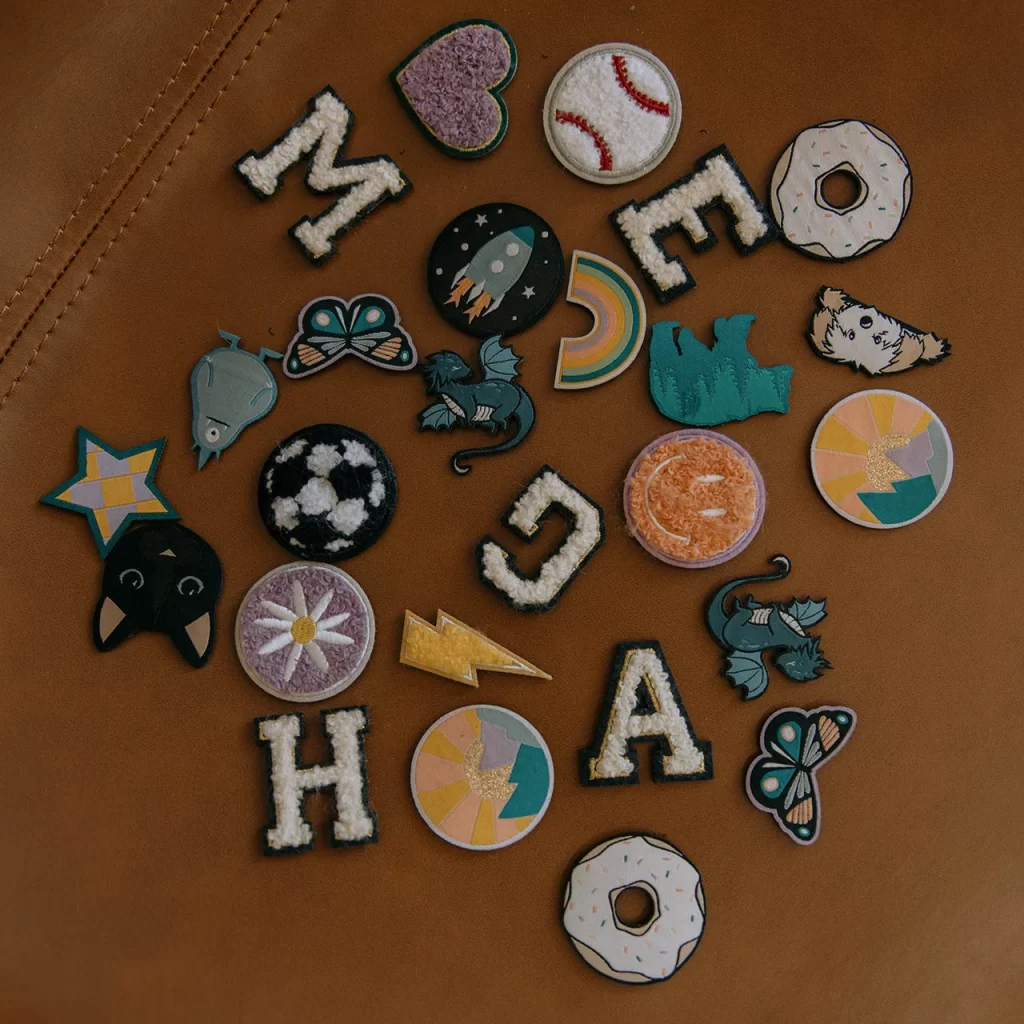 Image of many of the patches offered. They are spread out over a table. Some letters, cat, star, donut, butterfly, dragon, dog, etc.